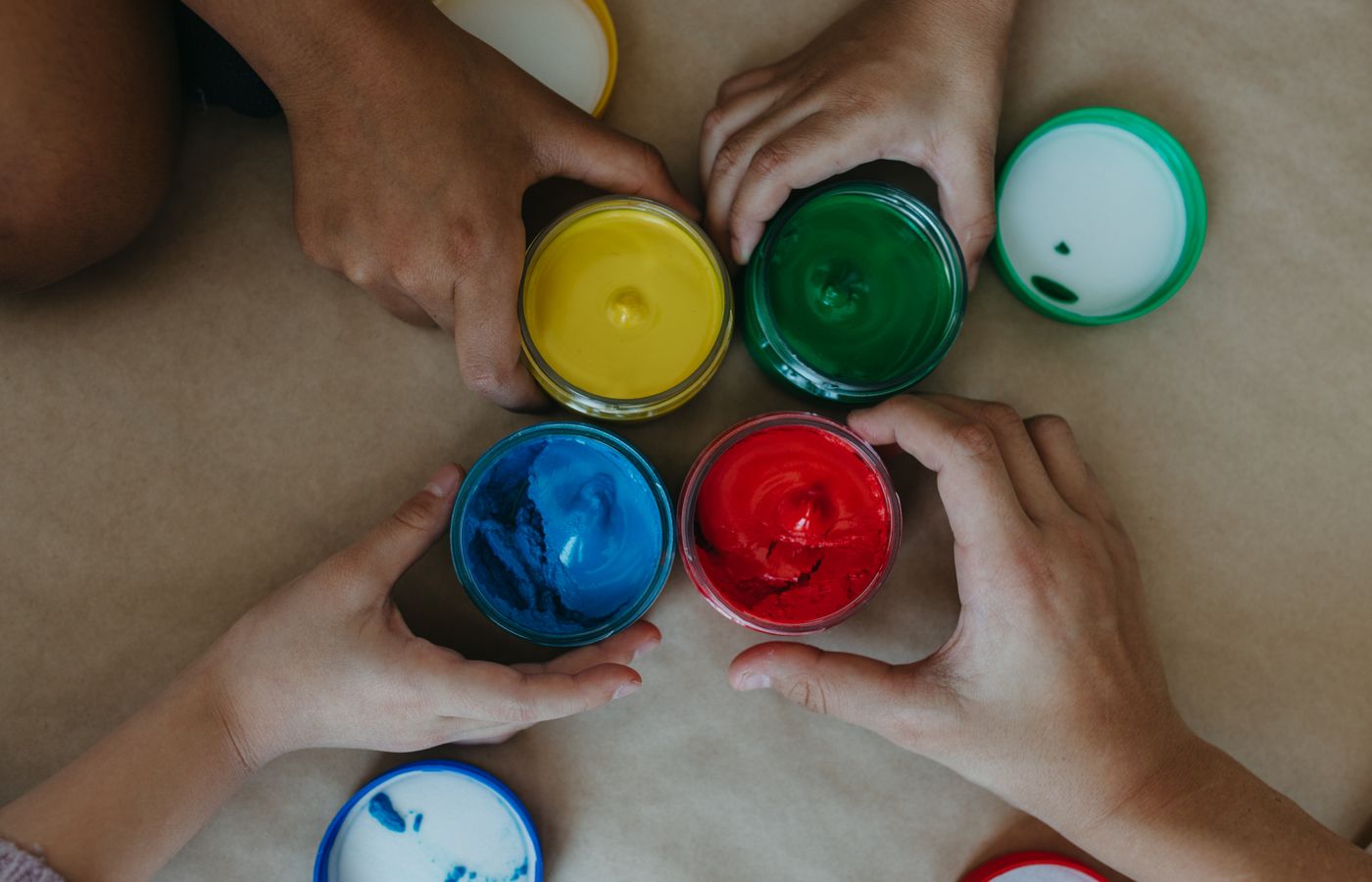 Top view of diverse hands holding colorful paint jars, showcasing creativity.