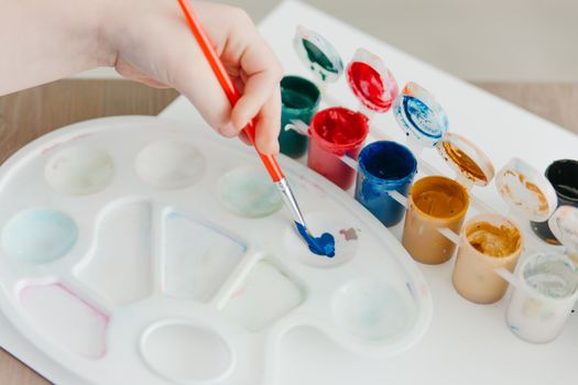 Close-up of a hand painting with vibrant acrylic colors on a palette, showcasing artistic creativity.