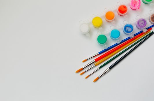 Flat lay of vibrant paints and brushes on a white background, perfect for art projects.