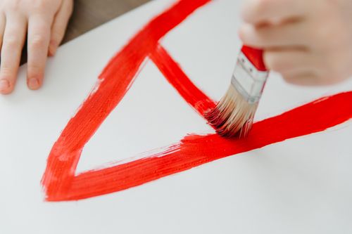 Free A child painting with red brush strokes on a white canvas, showcasing creativity and art education. Stock Photo