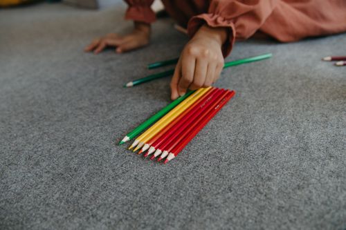 Free A hand organizes vibrant colored pencils on a carpeted floor. Stock Photo