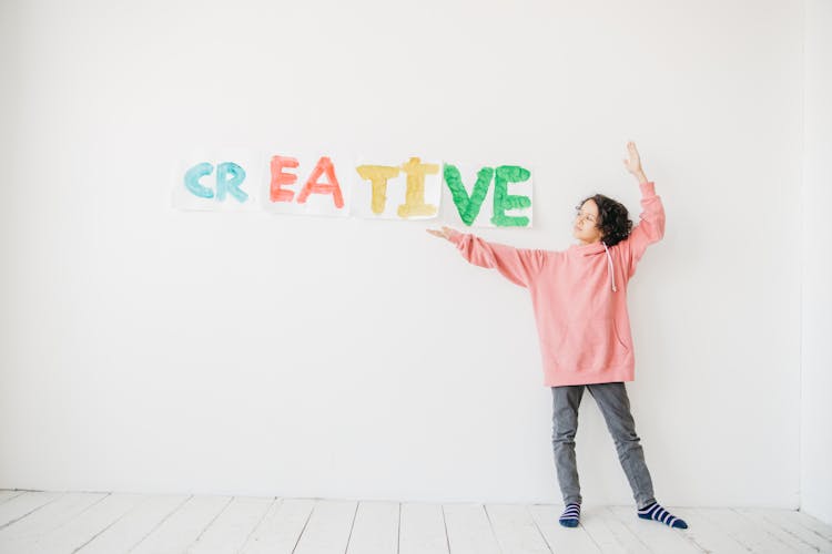 A Kid In Pink Hoodie Looking At The Artwork Posted On White Wall