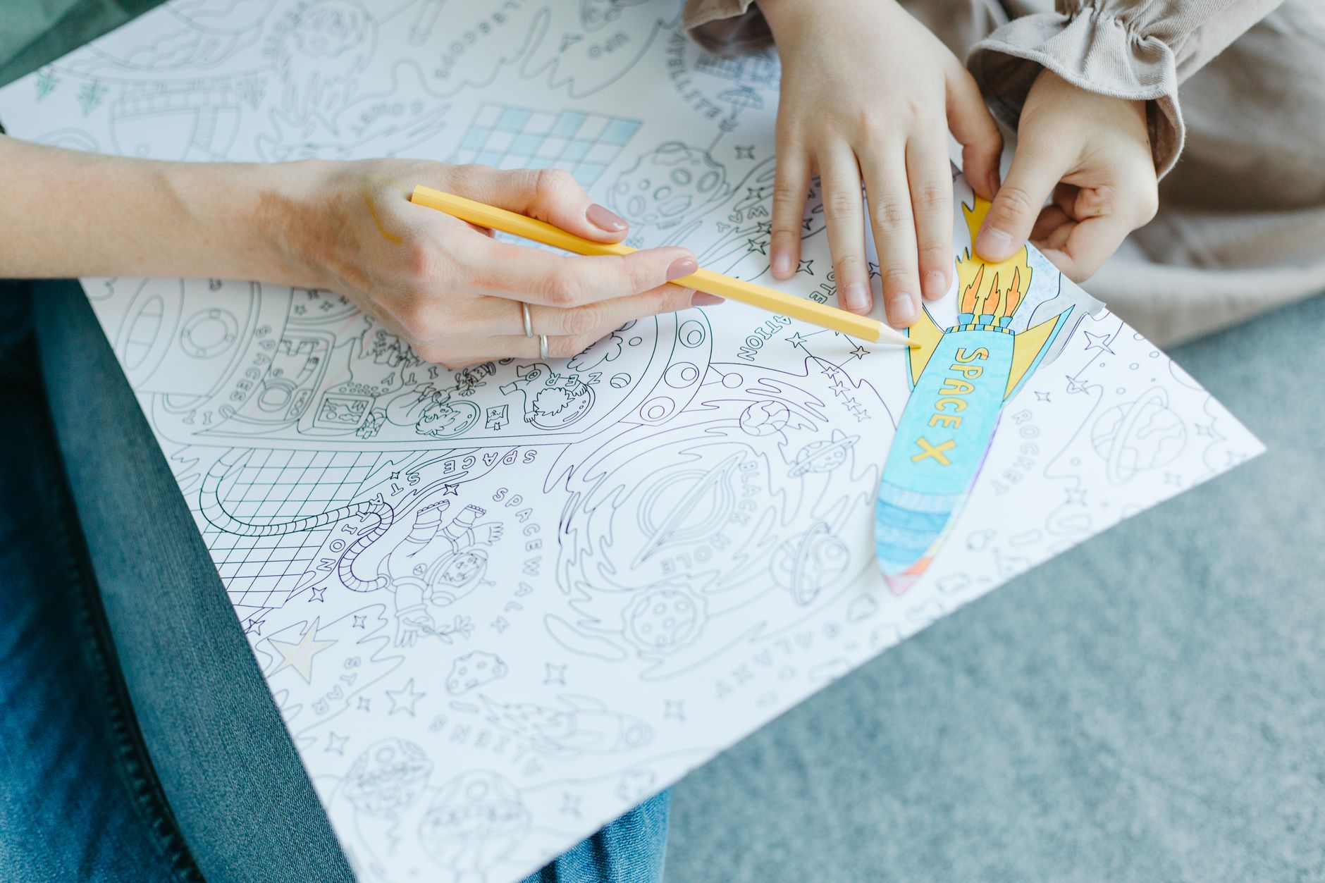 Close-up of hands coloring a space-themed drawing with colored pencils. Vibrant and interactive scene.
