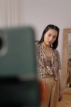Chic Asian woman poses for a selfie in a contemporary styled room.