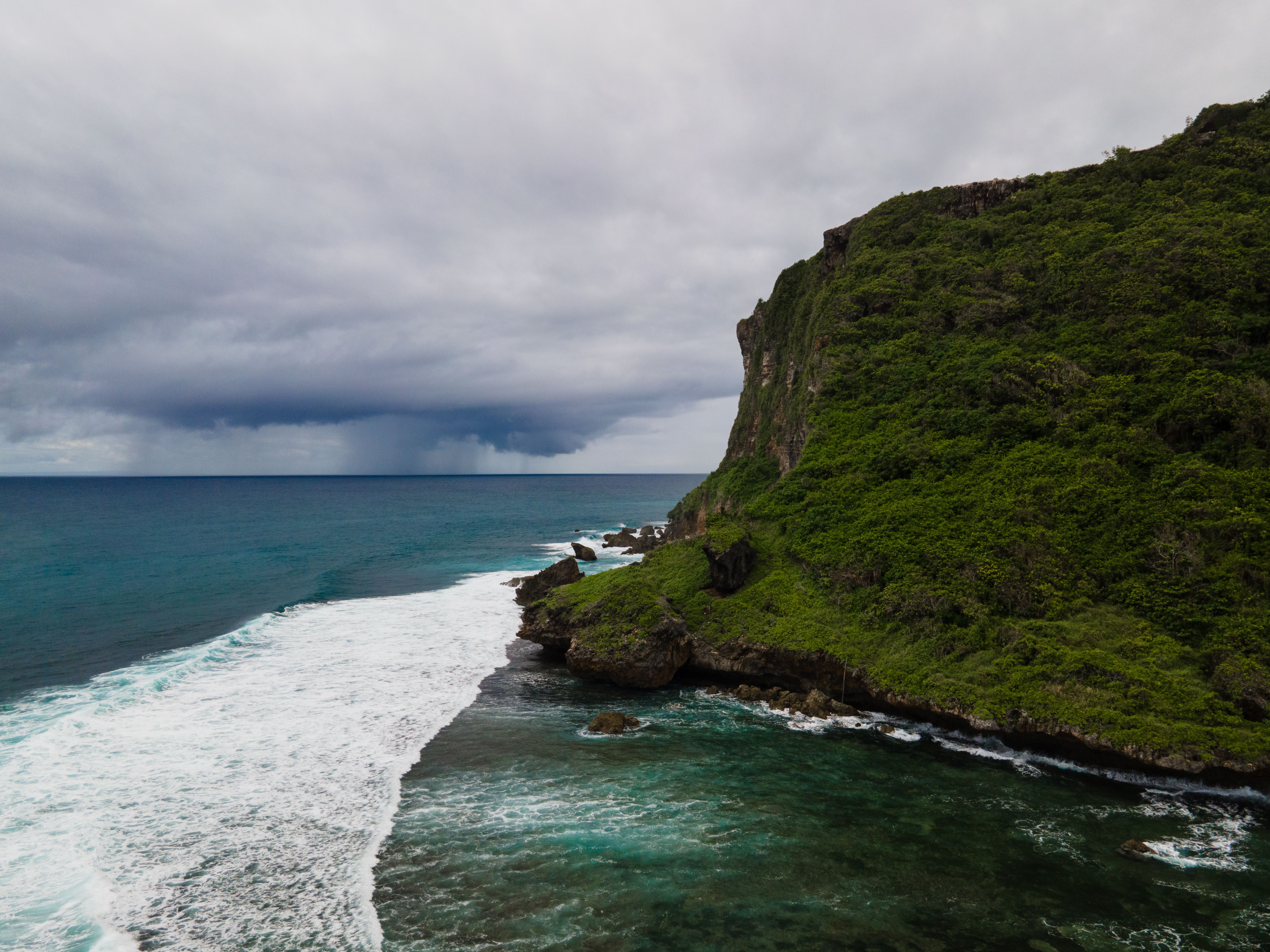 A stunning view of a rugged coastal cliff with waves crashing on the shore under a moody sky.