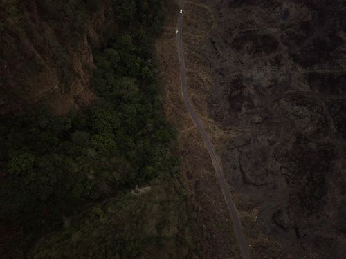 Free Aerial shot of a road dividing lush forest and barren volcanic terrain. Stock Photo