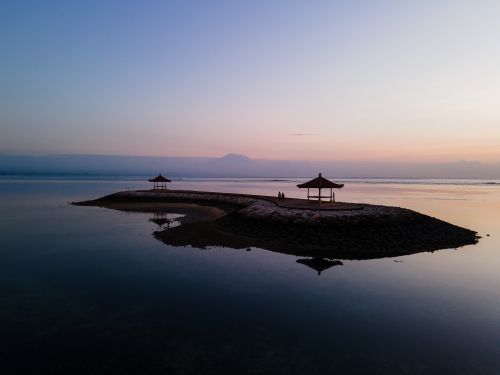 Free Peaceful scene of a sunrise over a tranquil seaside with gazebos and calm water. Stock Photo