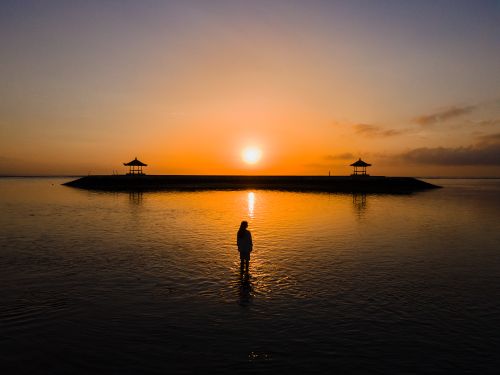 Free A captivating silhouette stands by the ocean at sunset with an island backdrop. Stock Photo