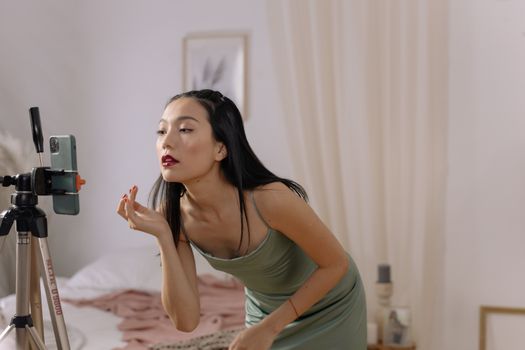 Asian woman applying lipstick while streaming live indoors.
