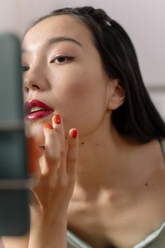 Close-up of an Asian woman applying lipstick with focus on her makeup and manicured nails.