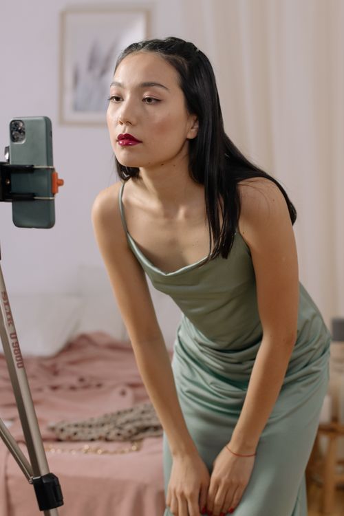 Free An Asian woman in a dress streaming live indoors using a cellphone. Stock Photo