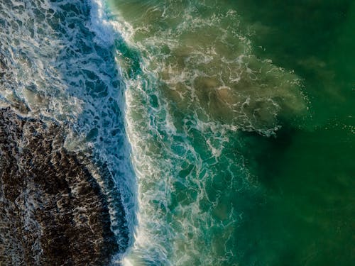Free Aerial Shot of Waves Crashing in the Sea Creating Sea Foam Stock Photo