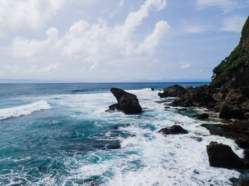 Free Waves crashing on rocky coast under blue sky with white clouds. Captures nature's drama and beauty. Stock Photo