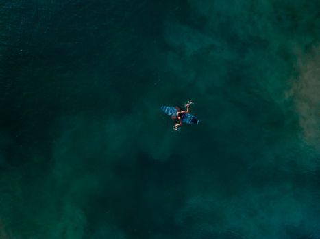 Aerial view of an unrecognizable surfer paddling on the deep blue ocean waters.