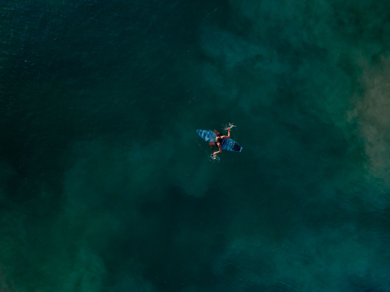 aerial view of an unrecognizable surfer paddling on the deep blue ocea