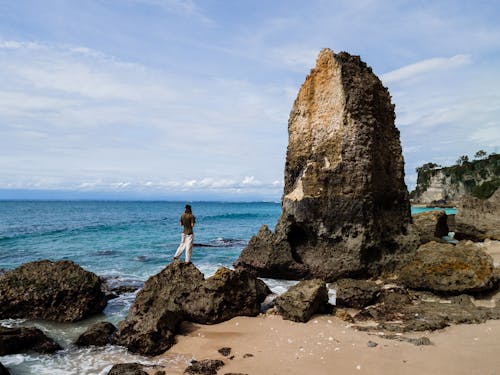 Free A Person Standing on a Rock Formation Near the Sea Stock Photo