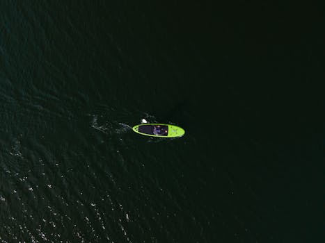 Drone shot capturing a surfer paddling on a vibrant green surfboard in dark ocean waters.