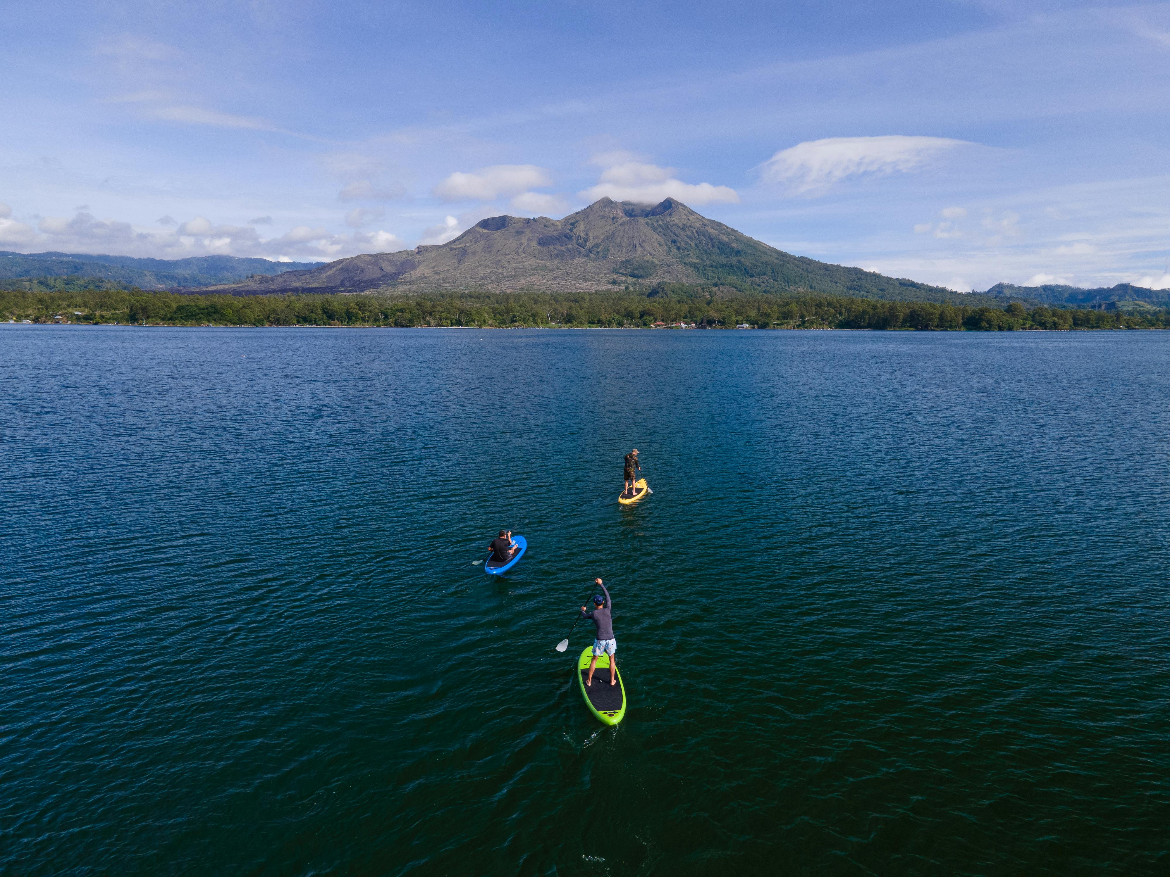 Aerial view of paddleboarders on a tranquil lake with mountain backdrop under blue skies.