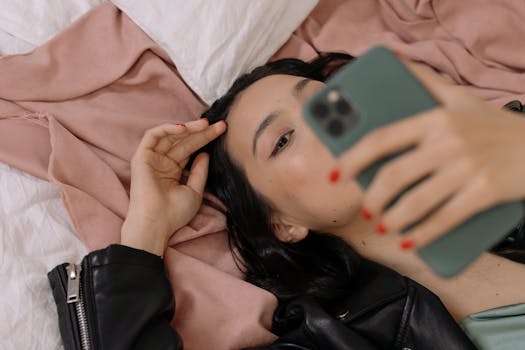 Woman in black leather jacket lying on bed, using smartphone with focus on personal relaxation.