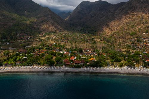 Free Stunning aerial view of a picturesque coastal village surrounded by dramatic mountains and serene seashore. Stock Photo