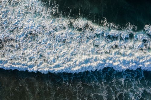 Free A stunning aerial shot capturing ocean waves crashing and forming sea foam at the shore. Stock Photo