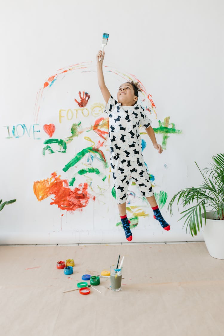 A Boy Jumping While Holding A Paint Brush