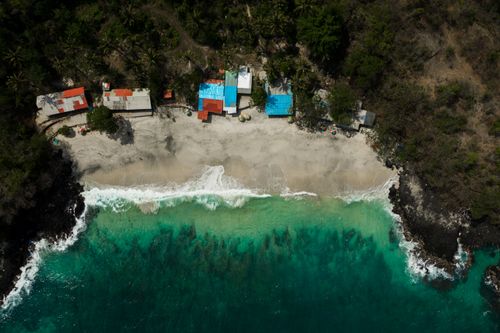 Free Aerial shot of secluded beach with rustic huts and vibrant blue water. Stock Photo