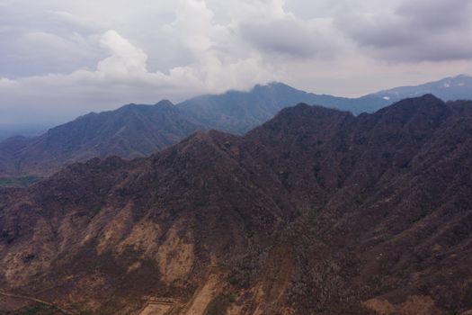 Dramatic aerial view capturing rugged mountain landscape under cloudy skies.