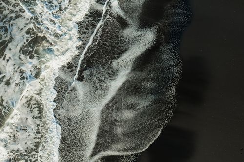 Free Drone shot capturing the dynamic movement of ocean waves crashing onto the beach shore. Stock Photo