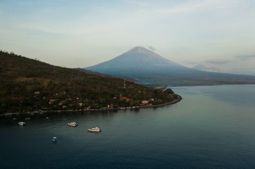 Free Breathtaking aerial shot of Bali's Mount Agung with tranquil coastal waters at sunrise. Stock Photo