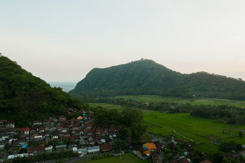 Free Aerial view of a serene village nestled between lush green hills and expansive fields at dawn. Stock Photo