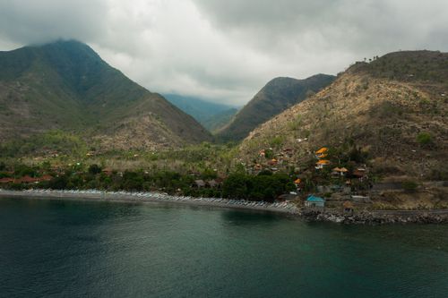 Free Drone shot capturing a tranquil coastal village nestled between mountains and a calm ocean. Stock Photo