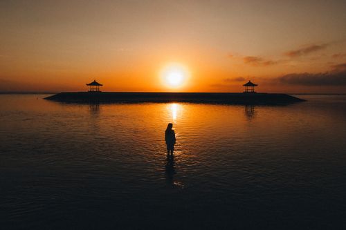Free A tranquil scene of a silhouette at sunrise near pavilions on a Bali beach. Stock Photo