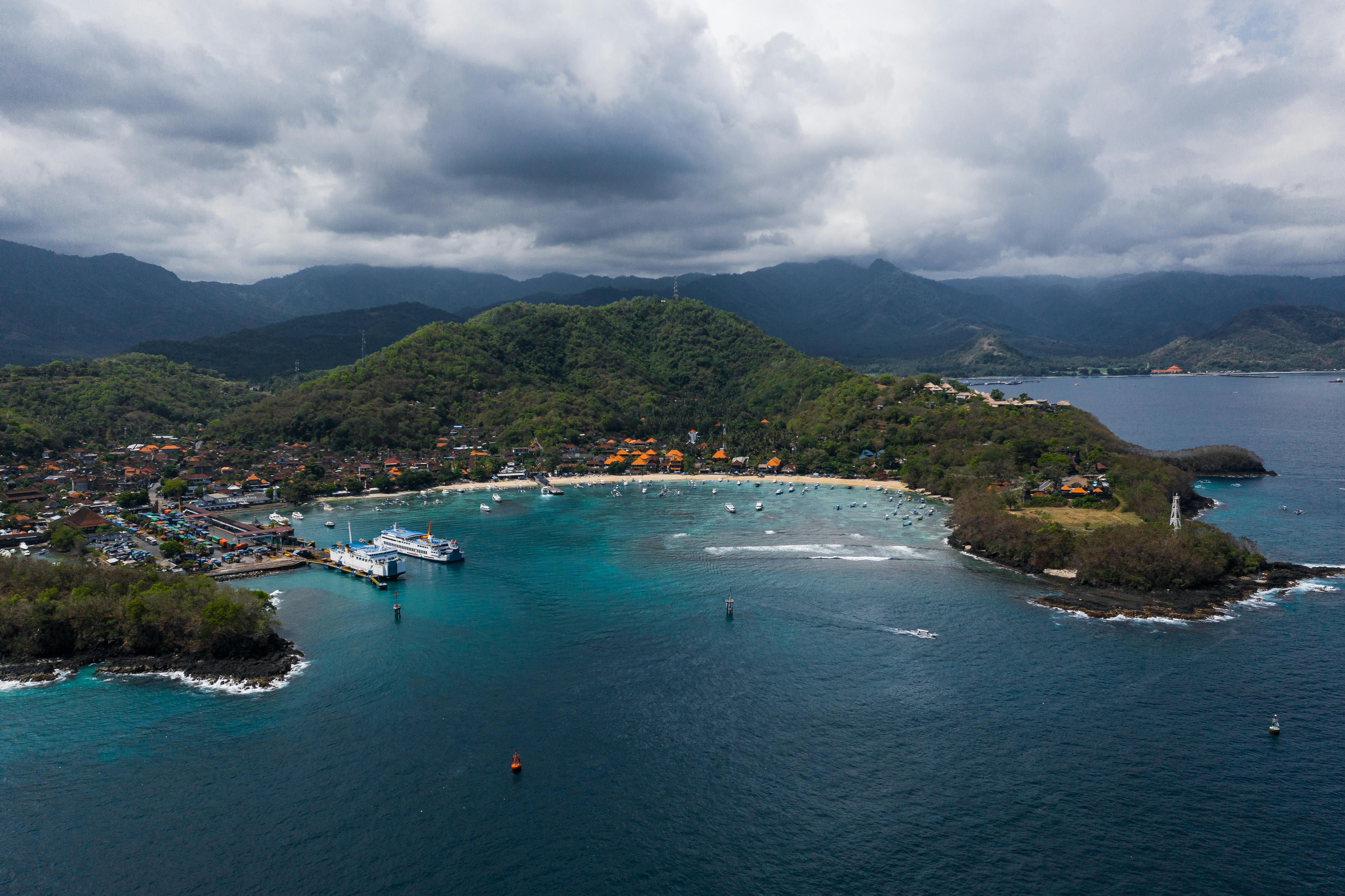 aerial view of boats on sea near green mountain under cloudy sky