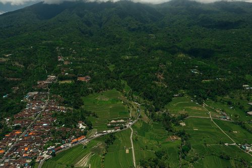 Free A stunning aerial view of vibrant green rice terraces and a nearby village surrounded by lush hills. Stock Photo