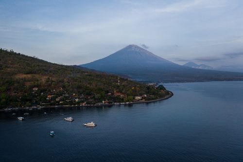 Free A serene aerial view capturing Mount Agung with boats on calm water at sunrise. Stock Photo