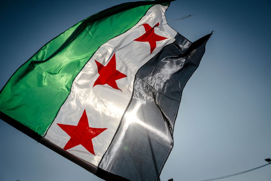 The Syrian independence flag waving vividly against a clear blue sky, capturing national pride in Idlib, Syria.