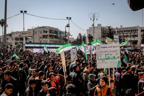 Free Protest in Idlib, Syria with people holding flags and banners in a city square. Stock Photo