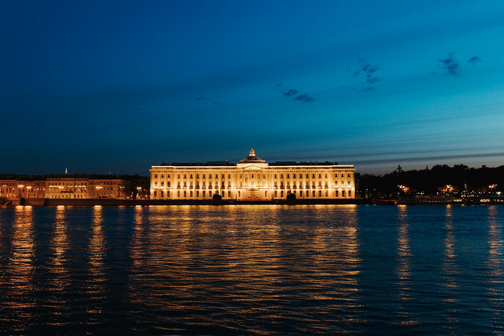 Illuminated Imperial Academy of Arts by the river in St. Petersburg at dusk.