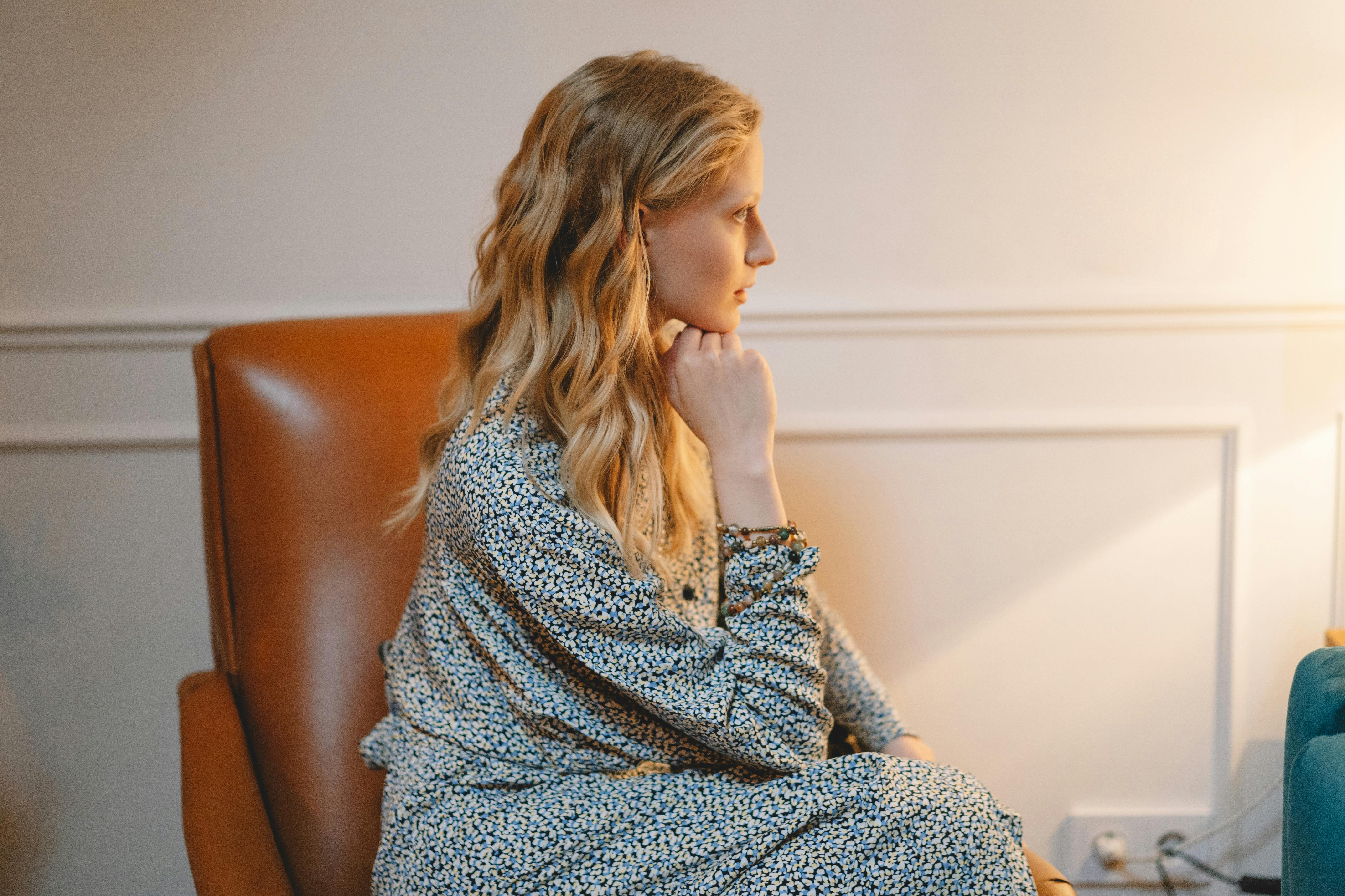 Profile view of a woman sitting thoughtfully indoors, illuminated by soft lighting.