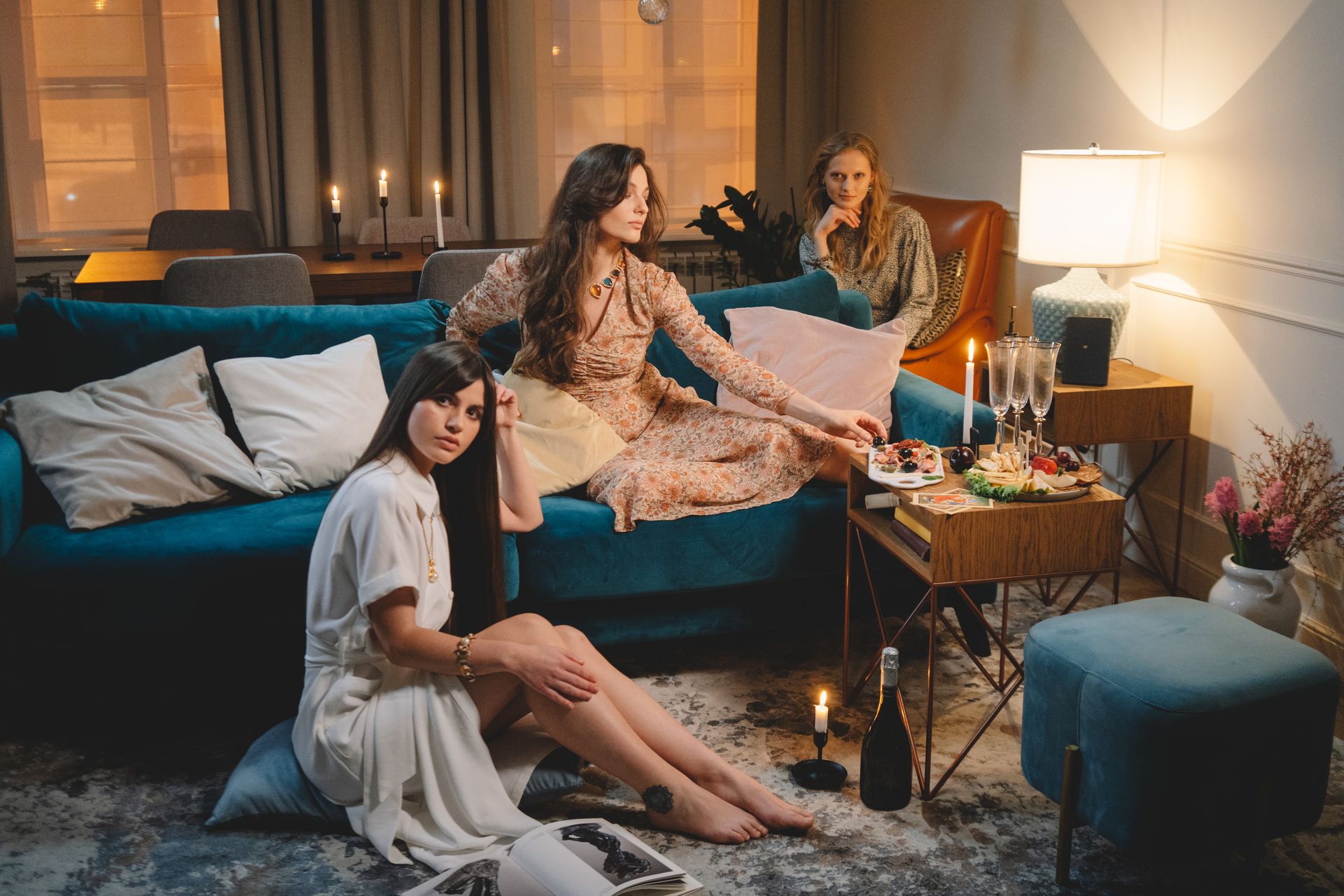 Three women enjoy a luxurious indoor gathering with wine and snacks by candlelight.