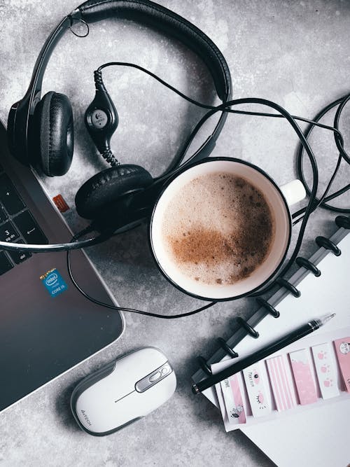 Free Top view of modern headphones placed on laptop near cup of latte and notebook with pen and stickers Stock Photo