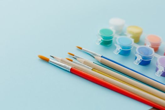 A collection of colorful paintbrushes and paints on a light blue background, perfect for art projects.