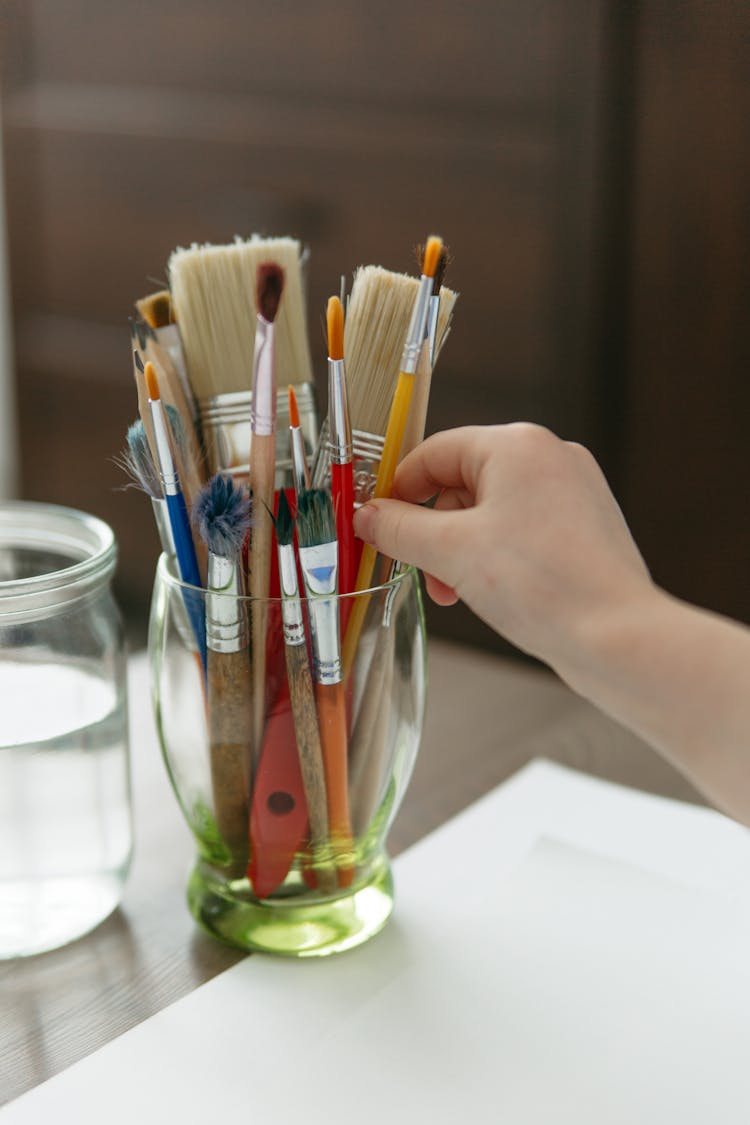 A Person Holding A Paint Brush In A Container