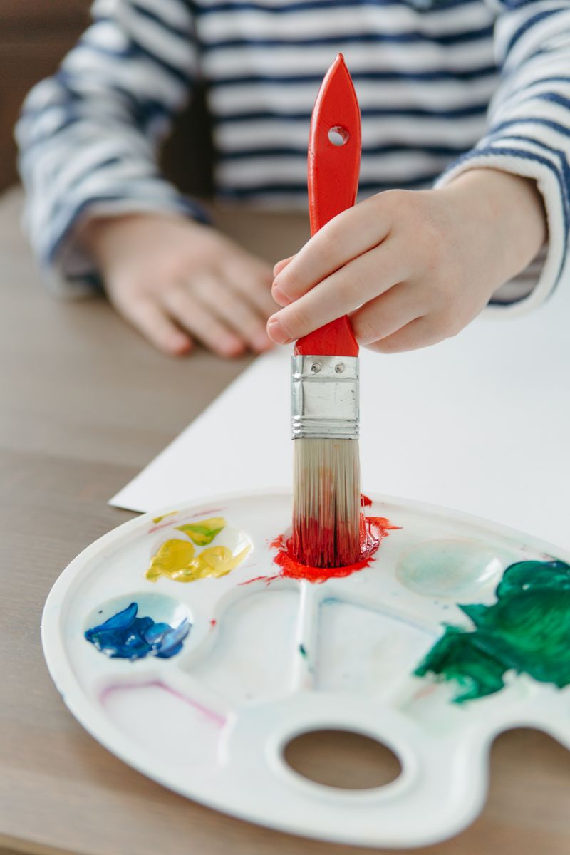 A child painting with a red brush and a palette of bright colours