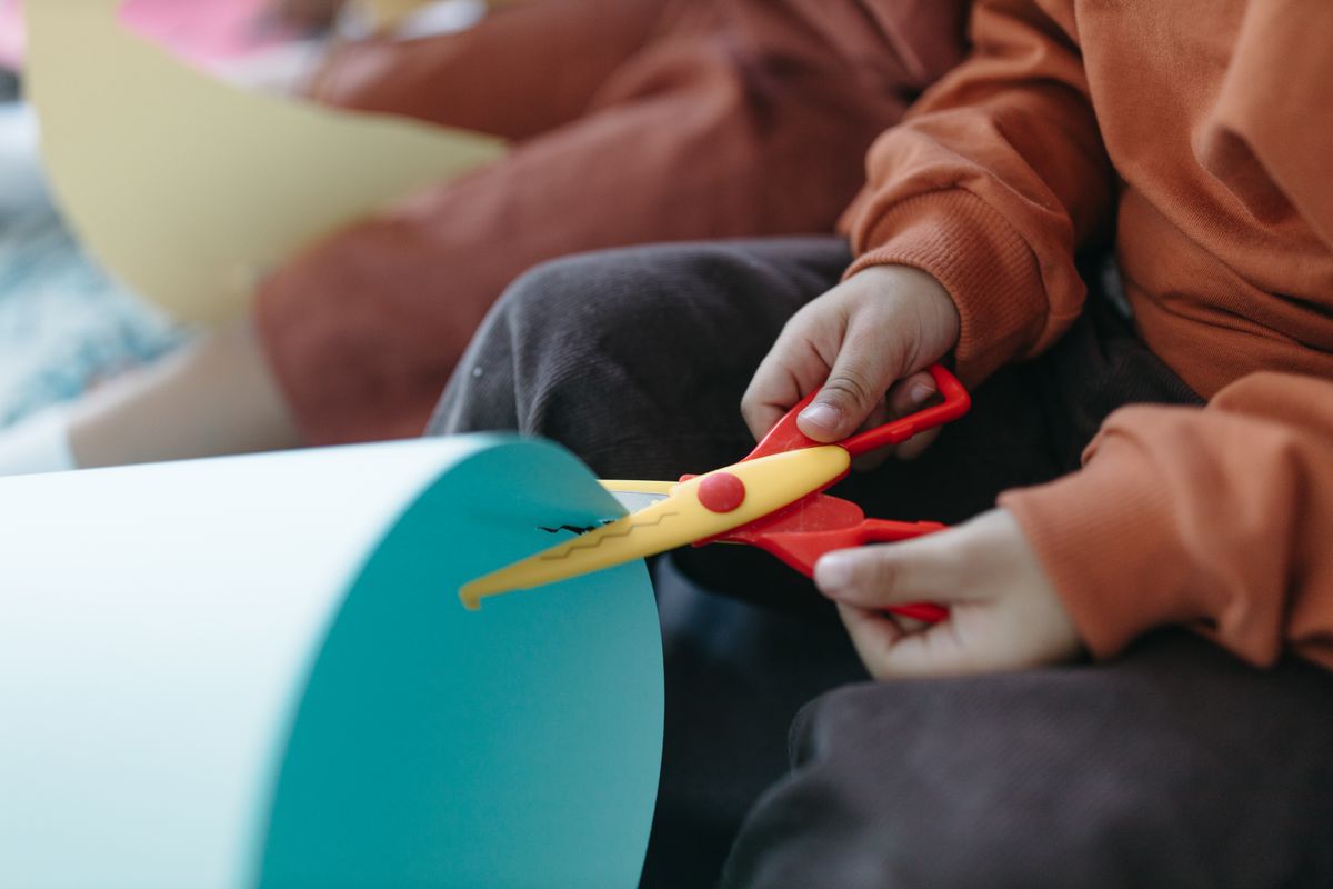 Close-up of small hands using colorful scissors to cut folded paper snowflakes