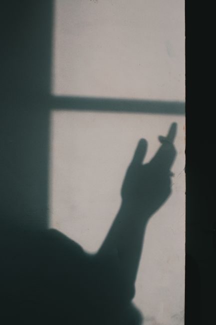 A shadow of a hand making a gesture on a wall, captured in soft, moody lighting.