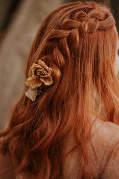 Red-haired woman with a braided hairstyle adorned with a dried flower, captured in a soft, warm tone.