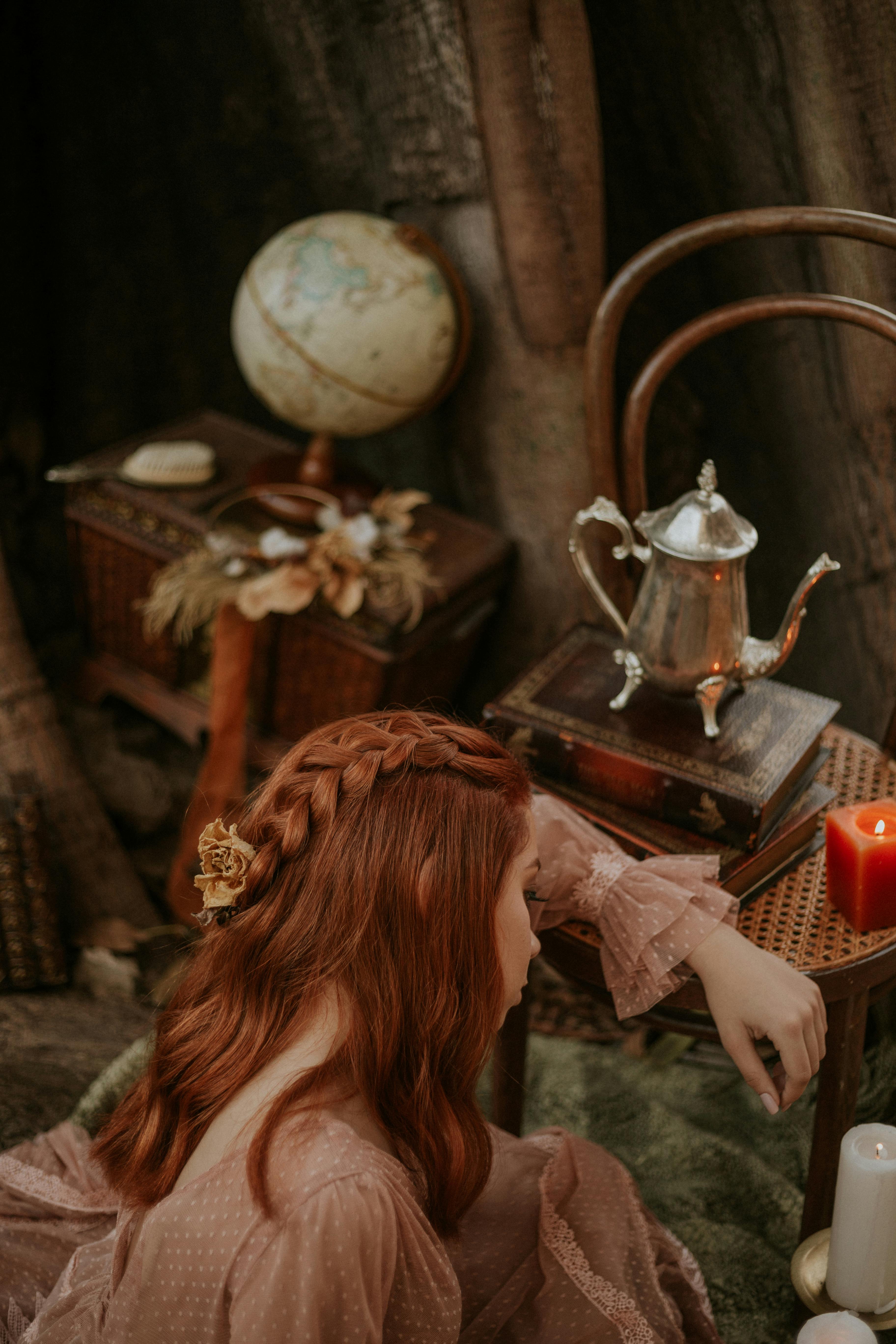 A redhead woman wearing a vintage dress in an antique setting with globe and teapot.