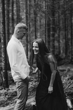 Joyful couple laughing together in a serene forest setting, black-and-white photography.